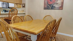 Ein Essbereich mit Holztisch und Stühlen, im Hintergrund eine Küche und ein Bild an der Wand.