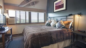 Ett hotellrum med en stor säng, ett skrivbord med en lampa, en tv och ett fönster med utsikt över landskapet.