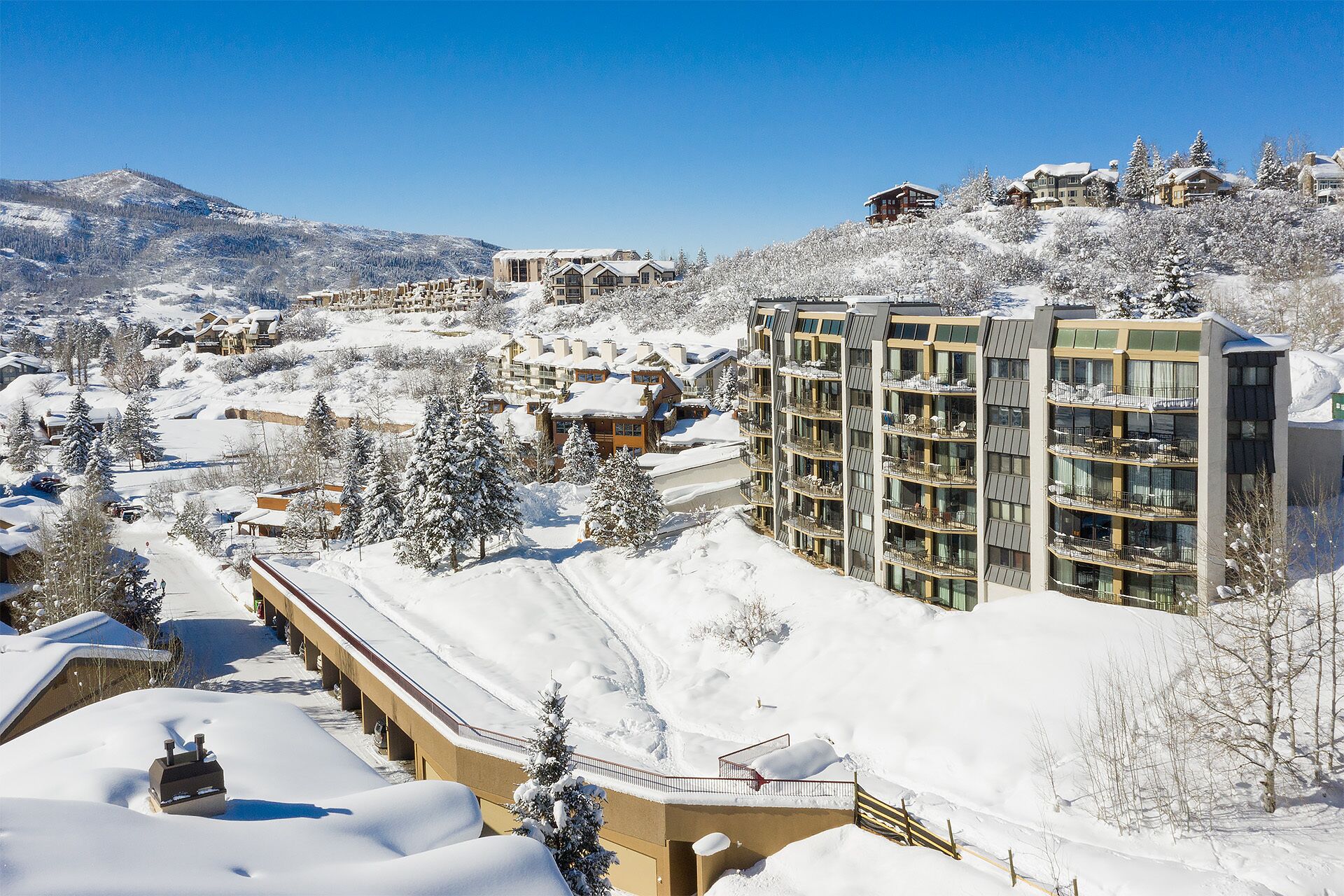 Un complejo turístico en la montaña, cubierto de nieve, con edificios de varias plantas, incluyendo un hotel con balcones y un telesilla.