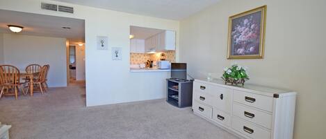A living room with a dining area, a kitchen in the background, and a white dresser with drawers.