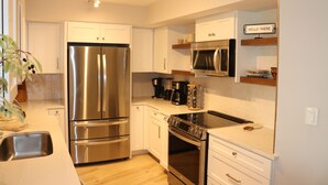 A modern kitchen with stainless steel appliances, white cabinetry, and a "HELLO THERE" sign. - El Matador 414 by Alicia Hollis Rentals FREE TICKETS! $300/Day (Fort Walton Beach)