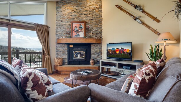 A cozy living room with a stone fireplace, a television, and a balcony with a view of the mountains. - RA304 | Beautiful Mountain and Valley Views | Fitness Center | Winter Shuttle (Steamboat Springs)