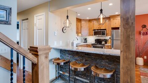 A kitchen with wooden cabinets, a stainless steel refrigerator, and a stone backsplash. - RA304 | Beautiful Mountain and Valley Views | Fitness Center | Winter Shuttle (Steamboat Springs)