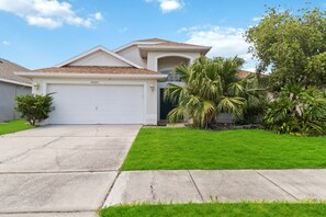 A two-story house with a garage, a well-maintained lawn, and a variety of tropical plants.