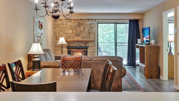 Ein gemütliches Wohnzimmer mit Kamin aus Stein, einem Esstisch mit Stühlen, einer Couch und einer Kandelaber.