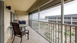 A balcony with a table and chairs, overlooking a beach and a building. - Slice Of Paradise (Sanibel)