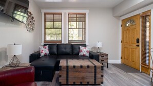 A living room with a black leather sofa, two windows with blinds, a wooden door, and a red chair. - Cozy Hotel Suite-Block from Main Street and Lift I Managed by Park City Lodging (PARK CITY)