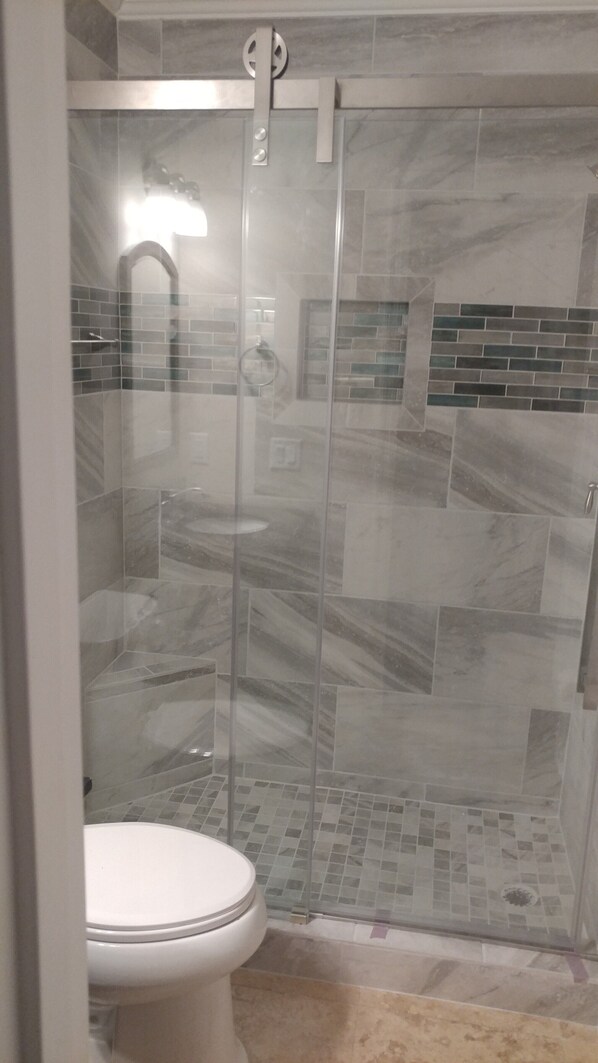 A bathroom with a glass-enclosed shower, a toilet, and tiled walls.