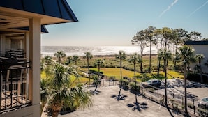 A view of a coastal property with a patio area, palm trees, and a clear sky.