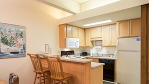 A compact kitchen with wooden cabinets, a microwave, a refrigerator, and a bar stool. - CA317 | Breathtaking Valley Views | Access to Outdoor Pool | Winter Shuttle (Steamboat Springs)