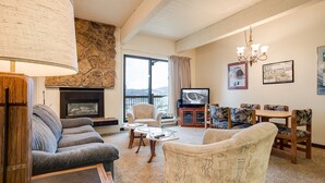A cozy living room with a stone fireplace, comfortable seating, a television, and a view of the outdoors. - CA317 | Breathtaking Valley Views | Access to Outdoor Pool | Winter Shuttle (Steamboat Springs)