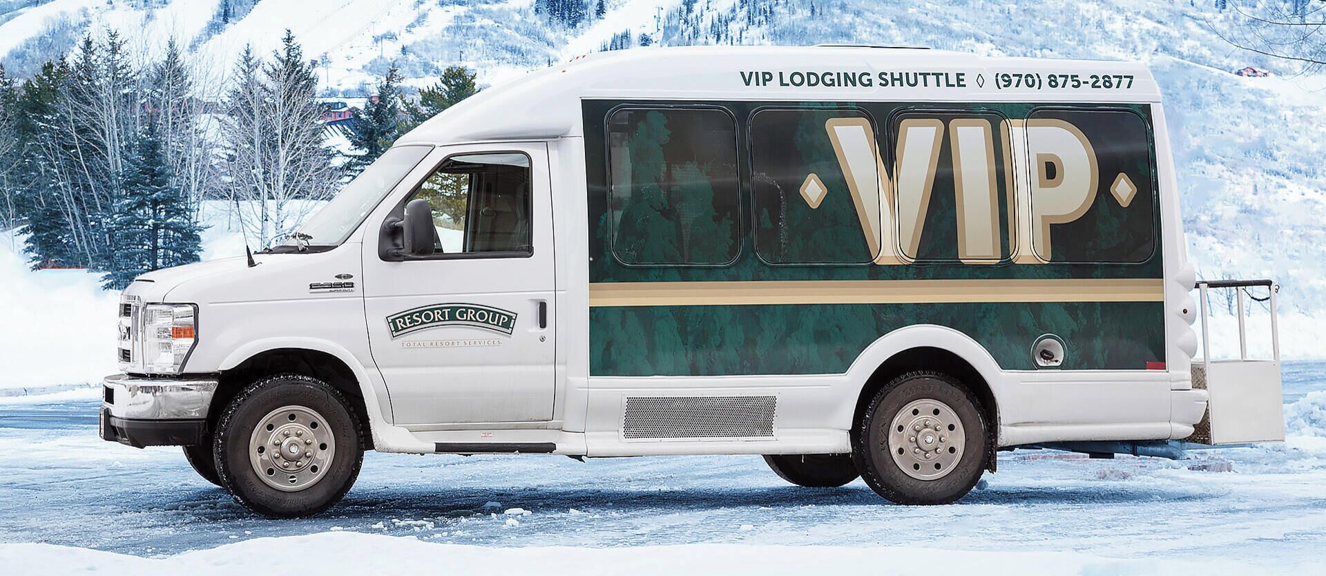 A white shuttle bus with 'VIP LODGING SHUTTLE' and a phone number on the side, parked on a snowy road.