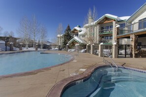 A pool area with a clear blue pool, a stone border, and a wooden deck.