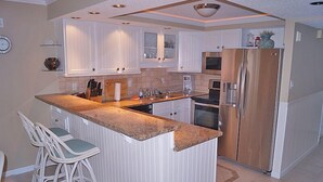 A kitchen with white cabinets, a granite countertop, a stainless steel refrigerator, and a built-in oven. - Ocean Hideaway 611-Oceanfront 18th St, Elev, W/D, AC (Ocean City)
