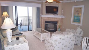 A living room with a fireplace, a television, and a balcony with a view. - Ocean Hideaway 611-Oceanfront 18th St, Elev, W/D, AC (Ocean City)