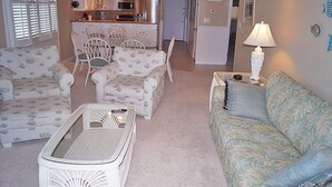 A living room with a sofa, chairs, a coffee table, and a kitchen in the background. - Ocean Hideaway 611-Oceanfront 18th St, Elev, W/D, AC (Ocean City)