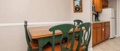 Un comedor con una mesa de madera y sillas verdes, un reloj en la pared y armarios de madera al fondo.