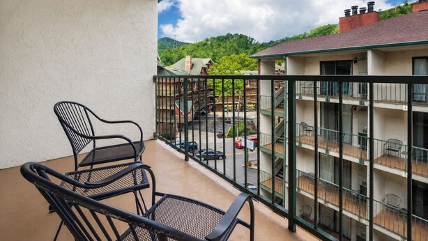 A balcony with two chairs, a view of a parking lot, and a building with multiple balconies.