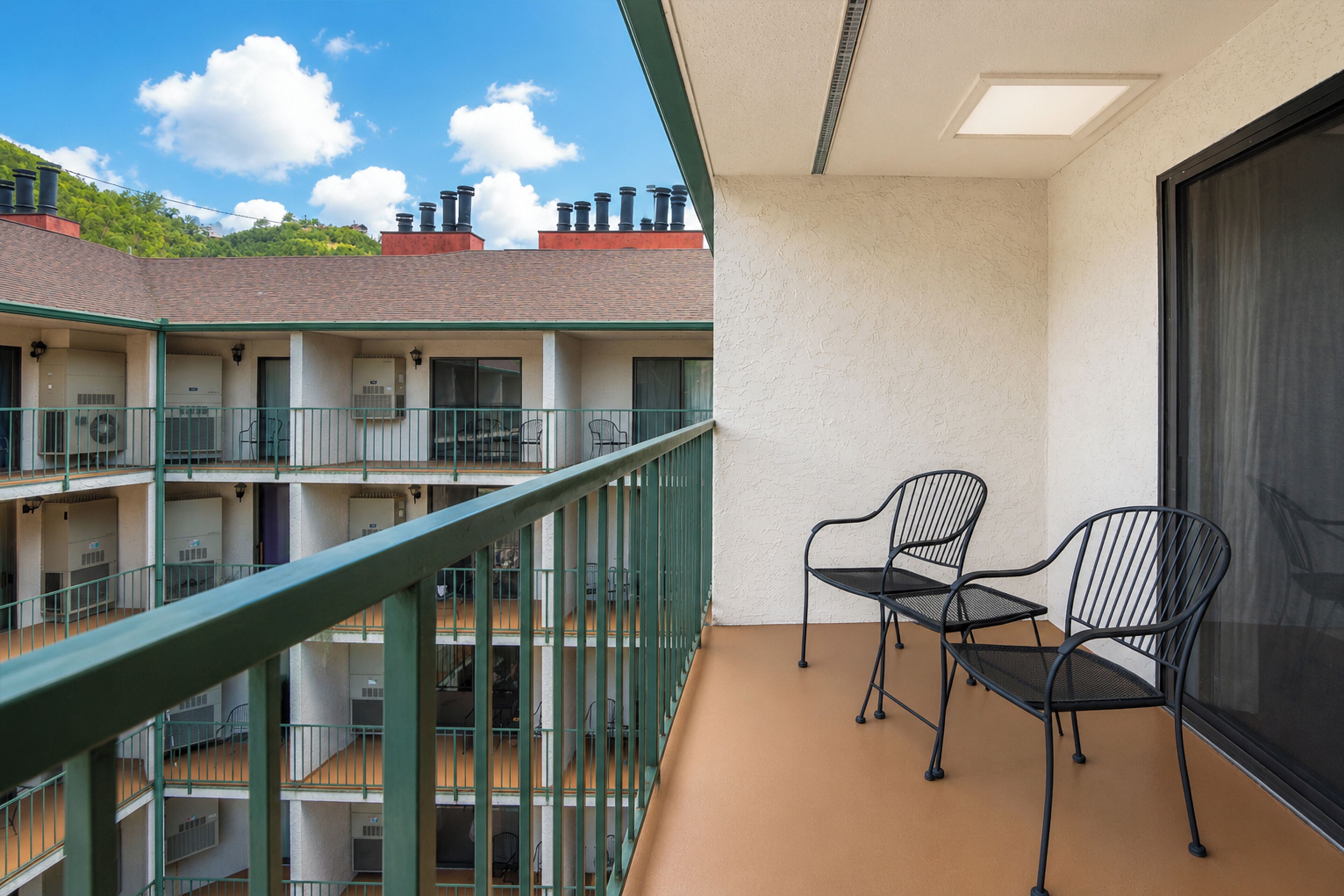 A multi-level hotel balcony with metal railings, a seating area with chairs, and a view of the surrounding buildings and sky.