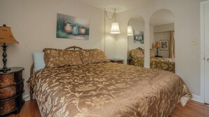 A bedroom with a large bed, a dresser, a lamp, and a painting on the wall.