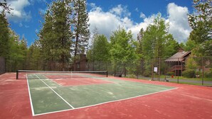 Un court de tennis avec un filet, entouré d’arbres et bordé d’un bâtiment en bois.