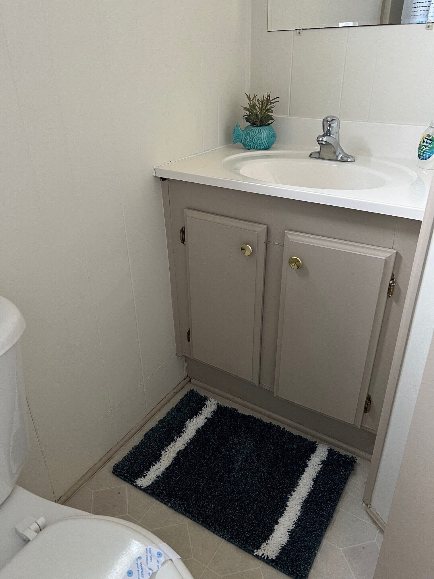 Un baño con un lavamanos blanco, una pequeña planta en maceta y un tapete a rayas negras y blancas.