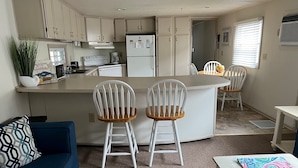 Una cocina compacta con una isla central, dos sillas blancas, un sofá azul y una mesa de comedor.