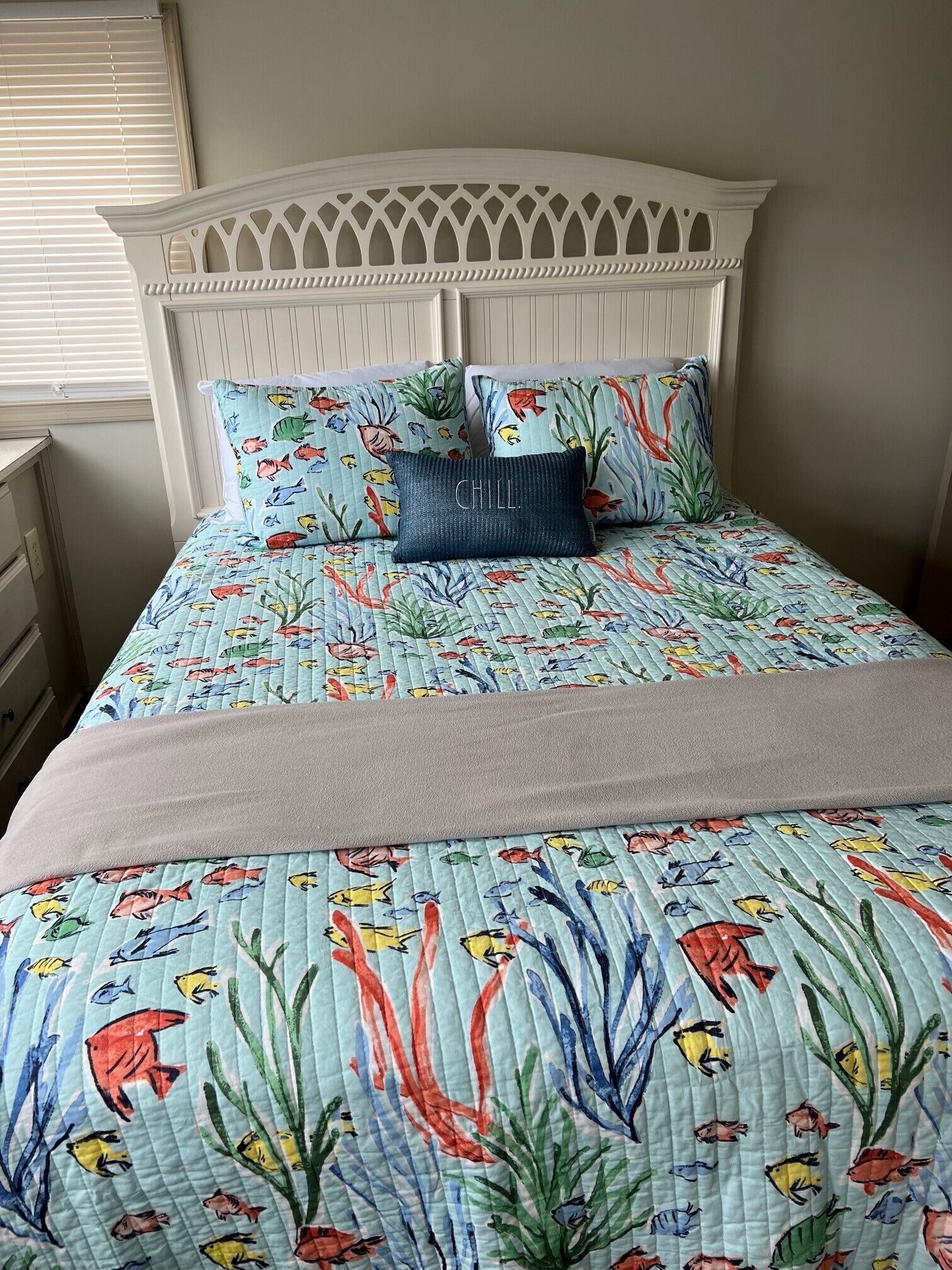 A bed with a quilted bedspread featuring a marine theme, a white headboard, and two pillows with a fish pattern.