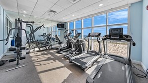 Ein Fitnessstudio mit Laufbändern, Crosstrainern und Kraftgeräten, große Fenster mit Blick auf den Strand.