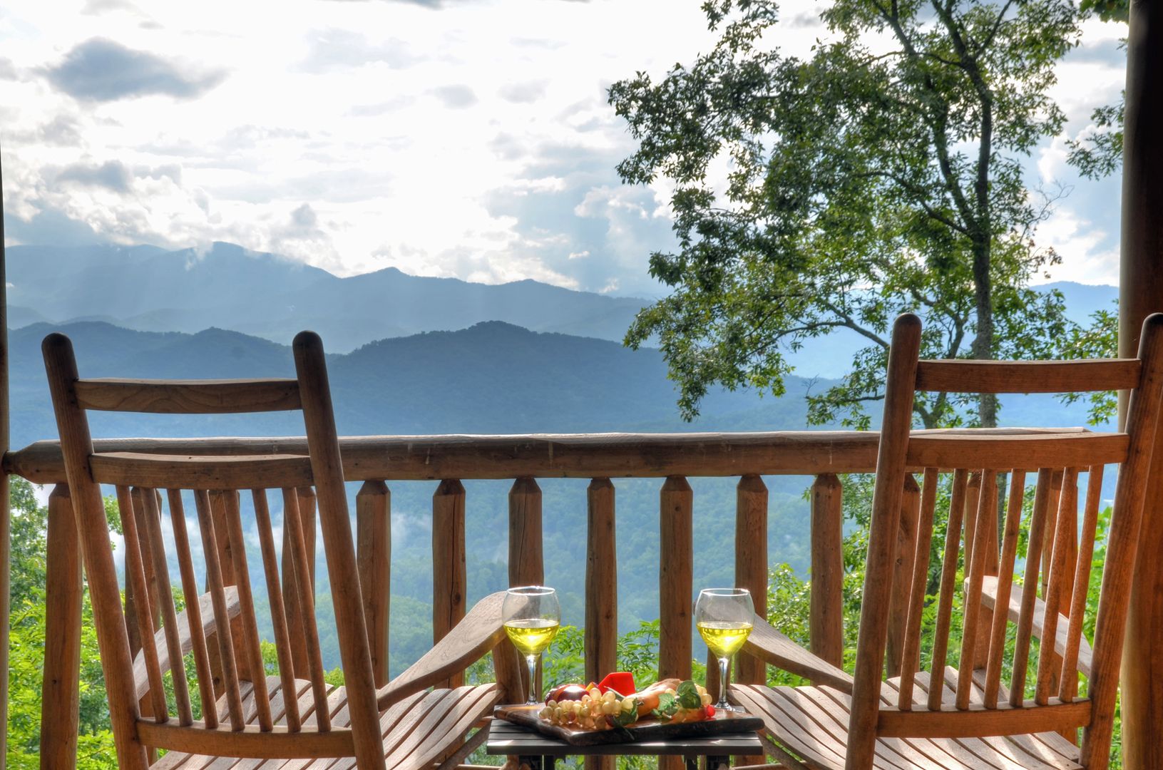 A wooden deck with two chairs and a table set for a meal, overlooking a mountainous landscape.