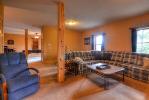 A living room with a sofa, armchair, and coffee table. There is a dartboard and a billiards table in the background. - 3BR log cabin, Hot Tub, sleeps 9, exceptional view + free railroad tix (Bryson City)