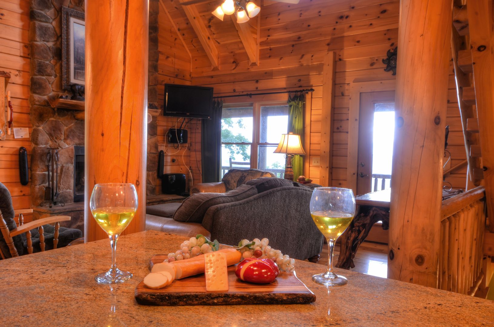 L’intérieur d’un chalet en bois présente une table à manger dressée pour deux personnes, deux verres de vin blanc, une planche à fromages avec divers fromages, et une tomate rouge.