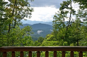 A wooden railing overlooking a mountainous landscape with dense foliage. - 3BR log cabin, Hot Tub, sleeps 9, exceptional view + free railroad tix (Bryson City)