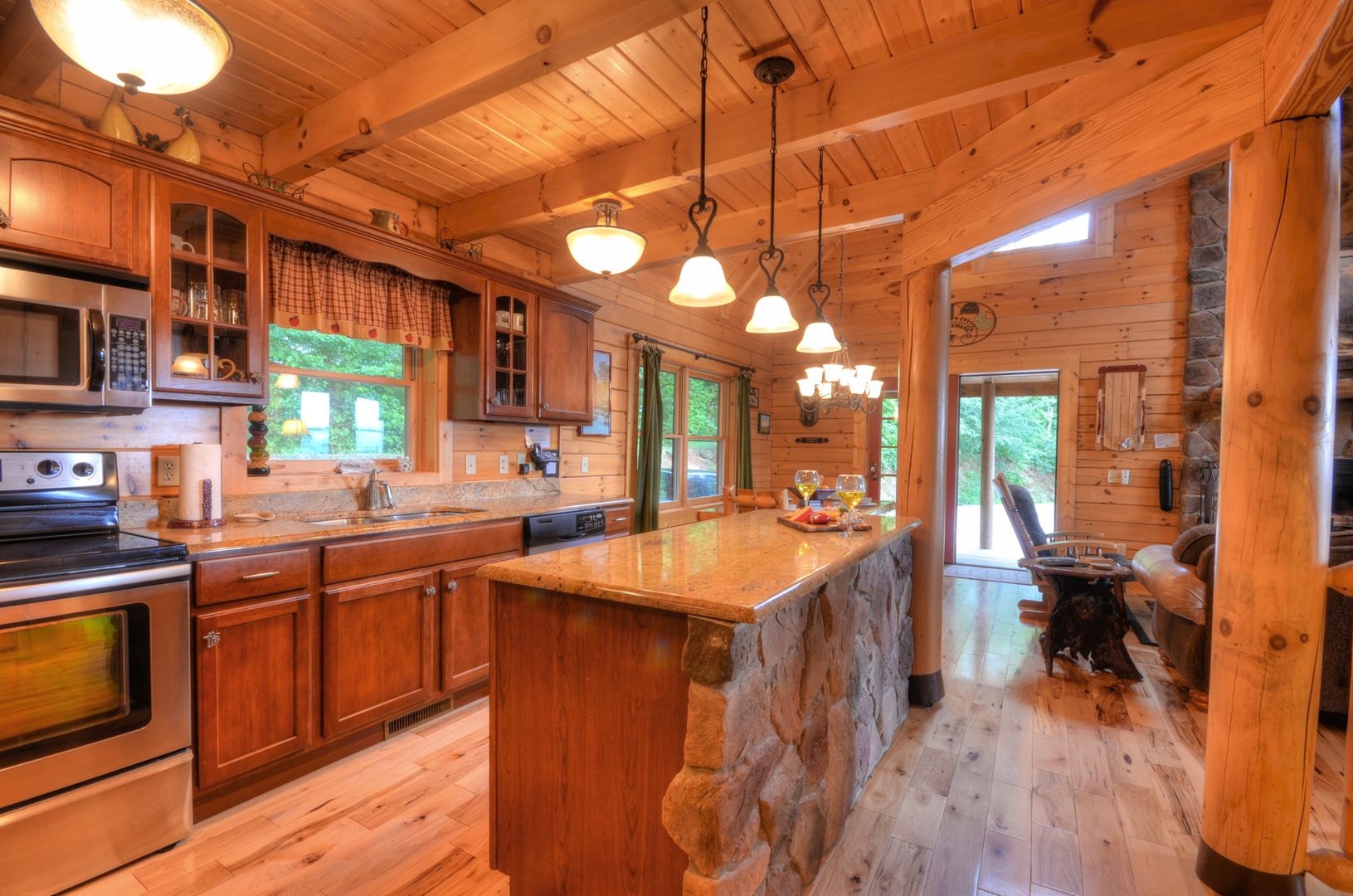 A wooden cabin interior with a kitchen, dining area, and a stone fireplace.