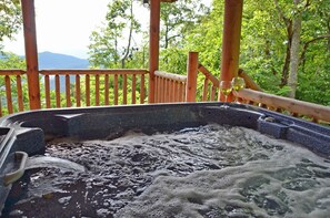 A hot tub with a wooden deck and a view of a forested area. - 3BR log cabin, Hot Tub, sleeps 9, exceptional view + free railroad tix (Bryson City)