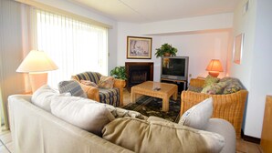 A living room with a sofa, armchairs, a coffee table, a television, and two lamps.