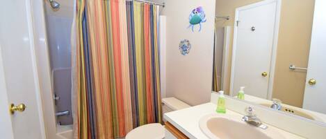 A bathroom with a shower curtain, toilet, sink, and mirror.