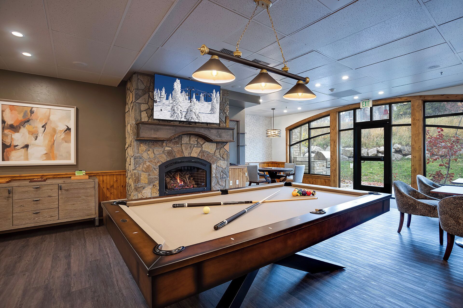 A pool table with a fireplace, a dining area, and a view through large windows.