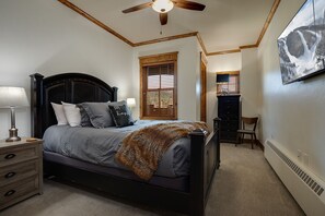 Cozy retreat with a dark bed frame, grey comforter, and a view of the surrounding landscape.