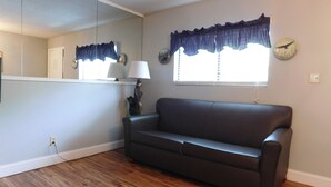 Una sala de estar con un sofá de color oscuro, una lámpara, una escultura decorativa de un oso y una ventana con un cortinero azul.
