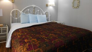 Una cama bien hecha con una colcha estampada, cabecera de metal blanco y dos lámparas de noche.