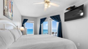 Ein Schlafzimmer mit einem großen Bett, einem Deckenventilator, einem an der Wand montierten Fernseher und Meerblick durch die Fenster.