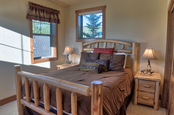 A bedroom with a wooden bed frame, two bedside tables with lamps, a window with a view of trees, and a wall-mounted shelf. - Breathtaking Ski & River View Chalet w/ Hot Tub (Breckenridge)