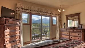 Une chambre dotée d’un grand lit, d’une commode en bois et d’un balcon offrant une vue sur la montagne.