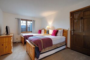 Ein Schlafzimmer mit zwei Betten, einer Holzkommode, einem Schreibtisch, einer Lampe und einem Fenster mit Vorhängen.