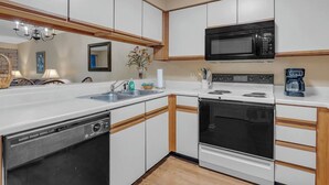 Una cocina con armarios blancos, un microondas negro, una estufa y un lavavajillas.