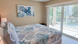 A bedroom with a bed, a nightstand, a painting of an octopus, and a balcony with a chair. - Taste Of Paradise (Sanibel)