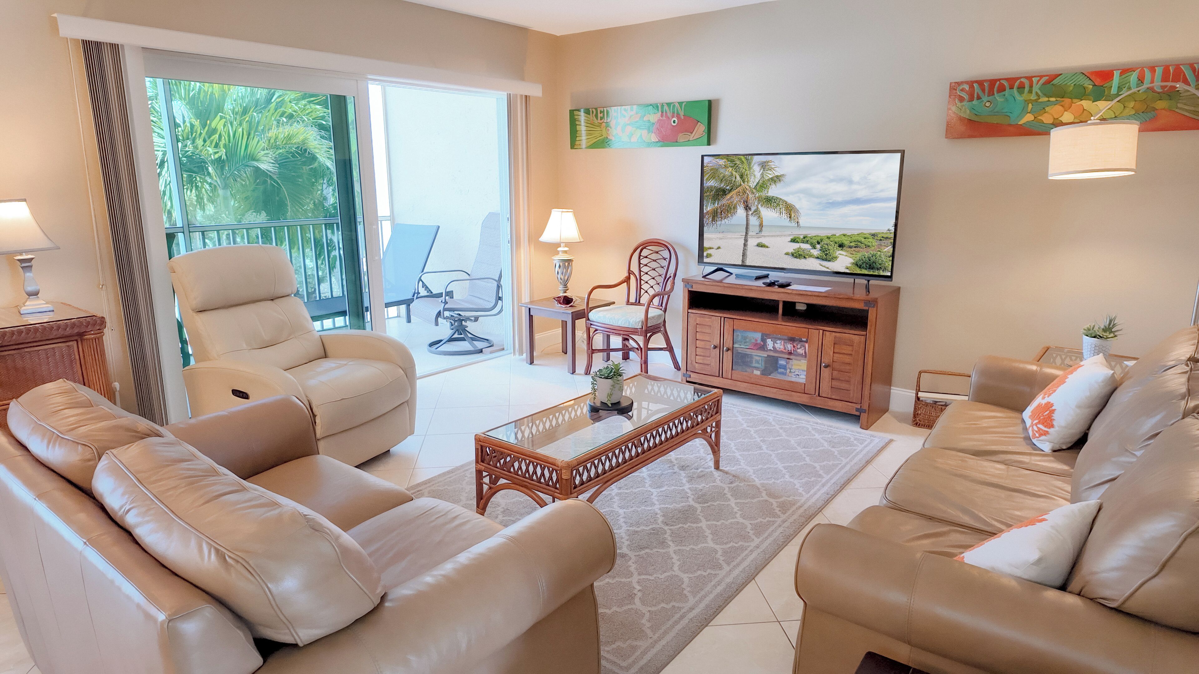 A living room with leather sofas, a glass coffee table, a TV, and a view of the outdoors.
