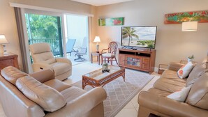 A living room with leather sofas, a glass coffee table, a TV, and a view of the outdoors. - Taste Of Paradise (Sanibel)