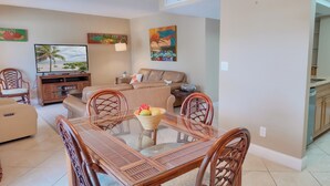 A living room with a TV, a sofa, a dining table with chairs, and artwork on the walls. - Taste Of Paradise (Sanibel)